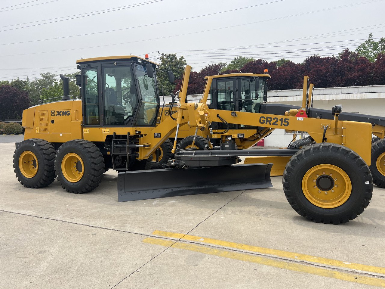 Side view of Brand New XCMG GR215 Motor Grader showing articulated frame, long chassis, and grading blade for road construction and leveling work
