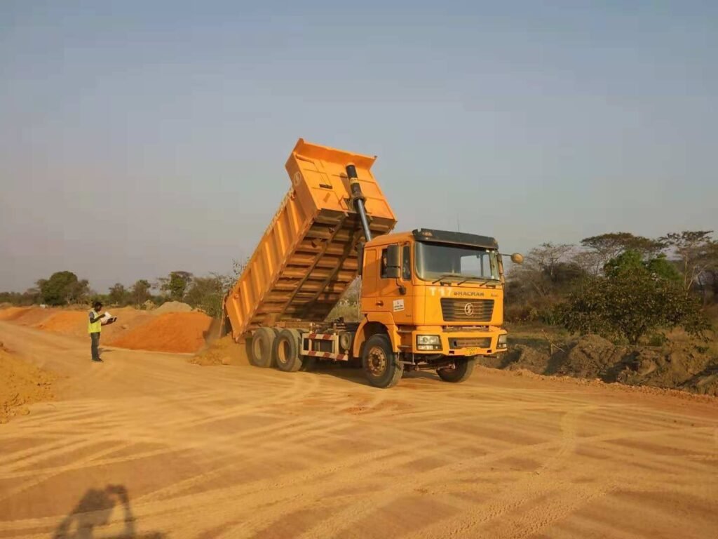 Shacman dump truck discharging cargo on a red mud road in humid tropical climate